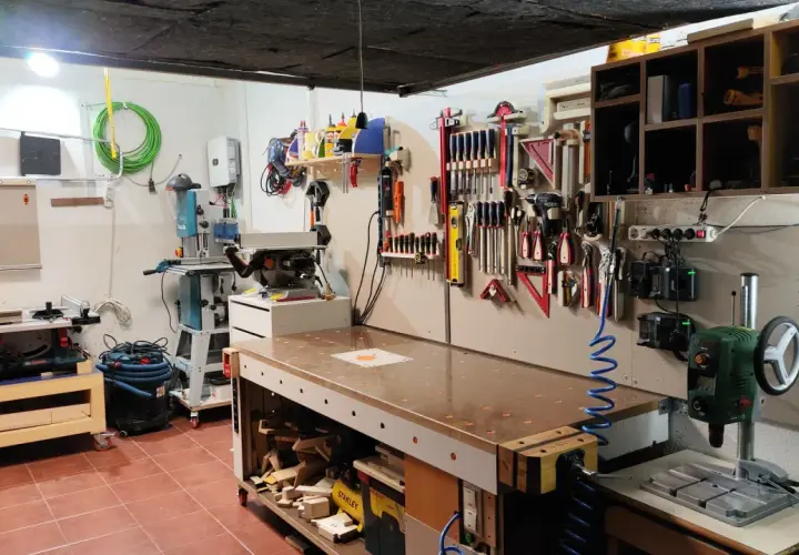 Un completo taller en casa con banco de trabajo, sierra de calar, taladro de columna y herramientas organizadas en la pared.