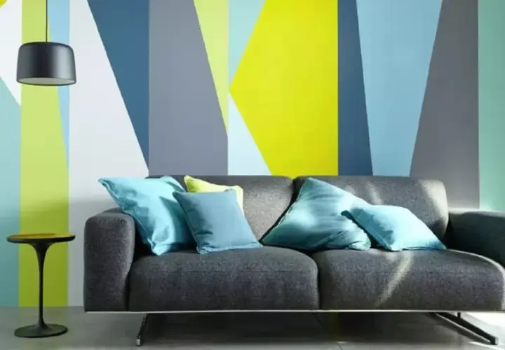 Sofá gris con cojines turques frente a pared con diseño geométrico en colores vivos. ¡Ideas para pintar paredes originales!