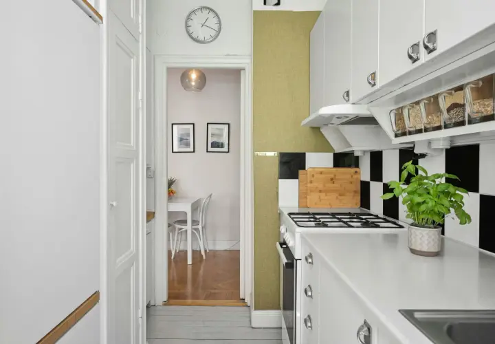 Cocina blanca y ordenada con estantes transparentes para organizar alimentos. Al fondo, un comedor pequeño.