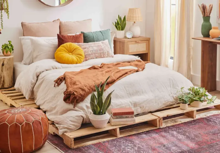 Cama acogedora con cómodas camas hechas con palets, cojines coloridos y manta naranja.