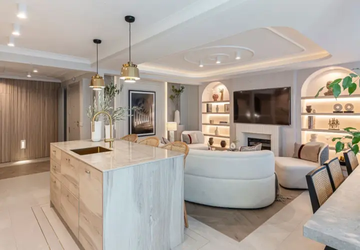 Cocina y sala de estar modernas con isla de mármol, sofás curvos y estanterías iluminadas. La iluminación ambiental crea una atmósfera acogedora, con suficientes **lúmenes por m2** para cada rincón.