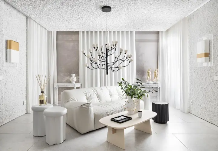 Salón minimalista con sofá blanco, mesa de centro ovalada y **gotele moderno** en paredes y techo. Lámpara escultural y cortinas blancas completan el espacio.