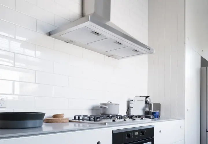 Cocina moderna con campana extractora de acero inoxidable, una de las muchas tipos de campanas extractoras. Encimera gris, vitrocerámica y nevera.