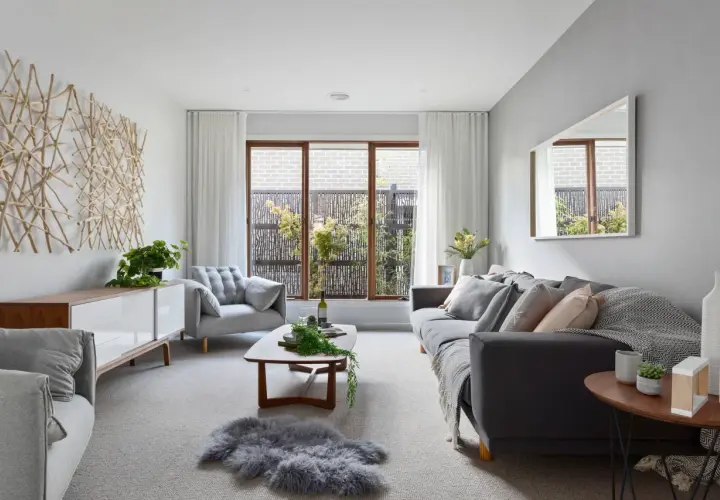 Salón moderno con sofás grises, mesa de centro de madera y arte de pared de ramas. Las paredes color gris crean un ambiente sereno.