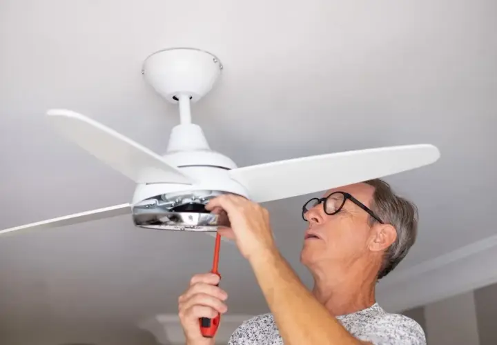 Hombre con gafas ajusta un ventilador de techo pladur con un destornillador.