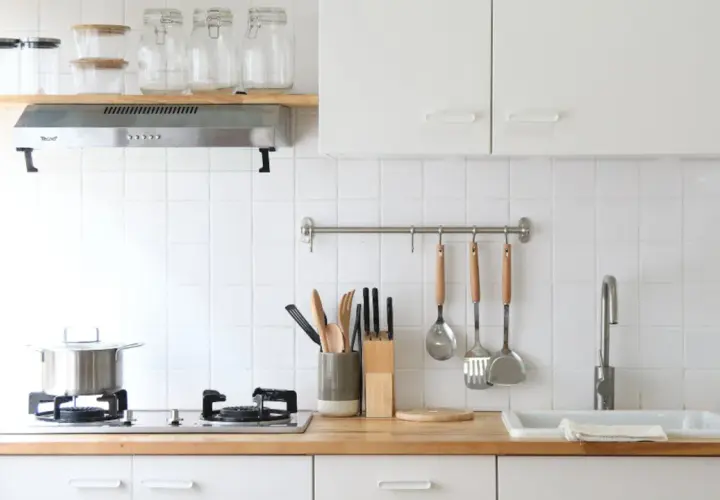 Una cocina pequeña y luminosa con encimera de madera, utensilios colgados y un fregadero.
