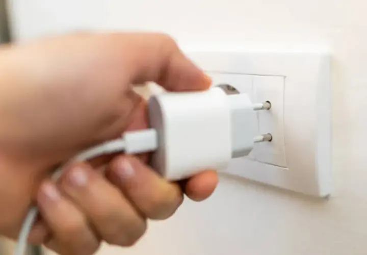 Mano insertando un cargador blanco en un enchufe de pared. Solución fácil de **enchufe sin obra** para cargar dispositivos.