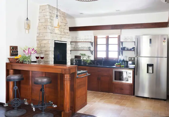 Cocinas con chimenea de piedra, barra de madera con taburetes, electrodomésticos de acero inoxidable y ventana rústica.
