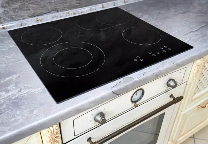 Placa de cocina vitrocerámica negra con cuatro zonas de calor y controles táctiles. Encimera gris piedra.