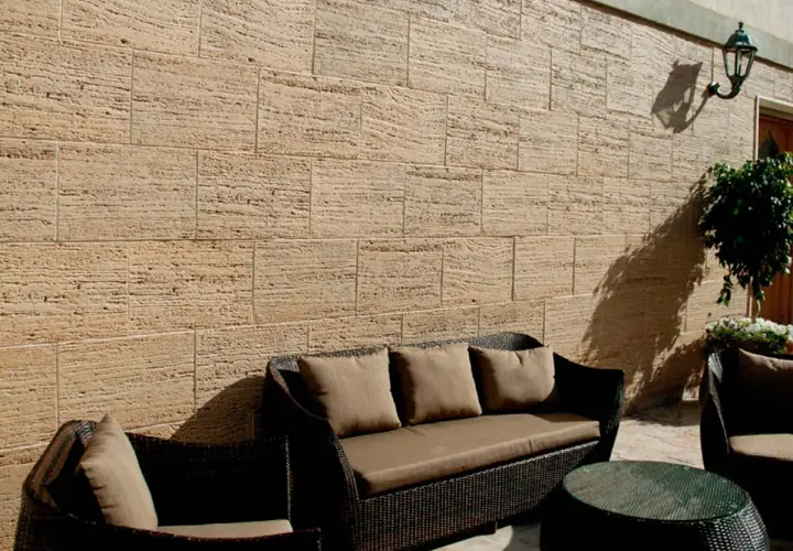 Un patio acogedor con muebles de mimbre y cojines marrones, rodeado de patios con paredes de piedra natural.