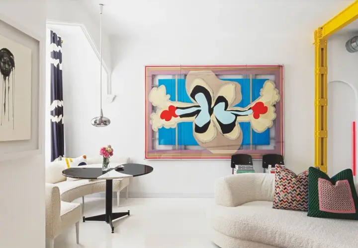 Un salón moderno con arte abstracto y muebles curvos. Sofás blancos texturizados y una mesa redonda negra y blanca crean sencillas salas pequeñas.