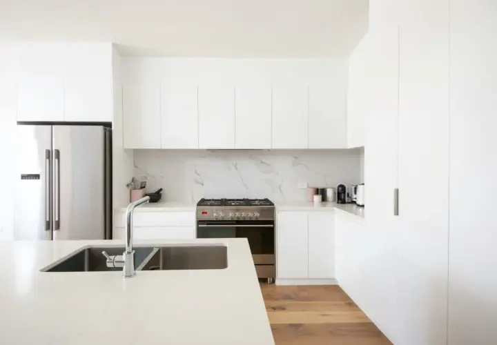 Cocinas modernas blancas con electrodomésticos de acero inoxidable, encimera de cuarzo y suelo de madera.