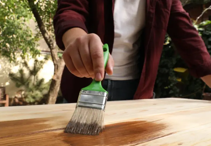 Persona aplica protector a madera con brocha verde. Aprende como impermeabilizar madera para protegerla.