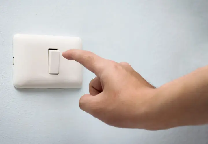 Dedo presionando un conmutador blanco en una pared azul claro.