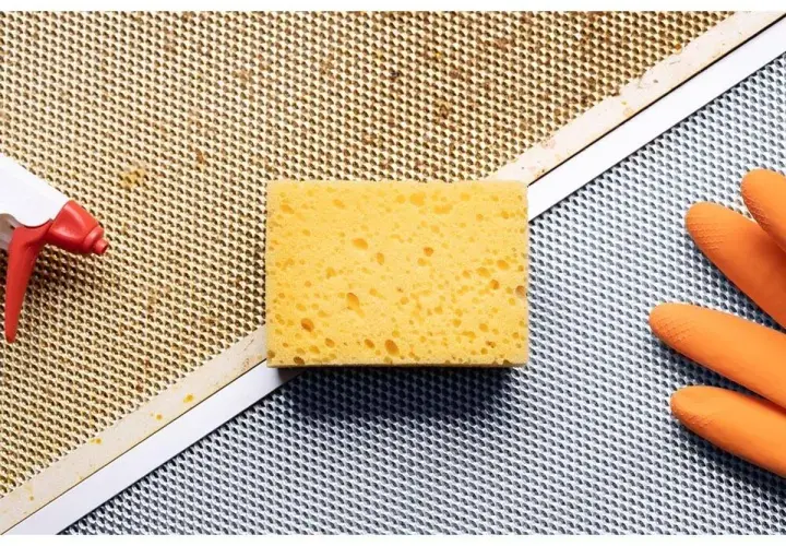 Esponja, guantes naranjas y spray listos para limpiar extractor cocina.