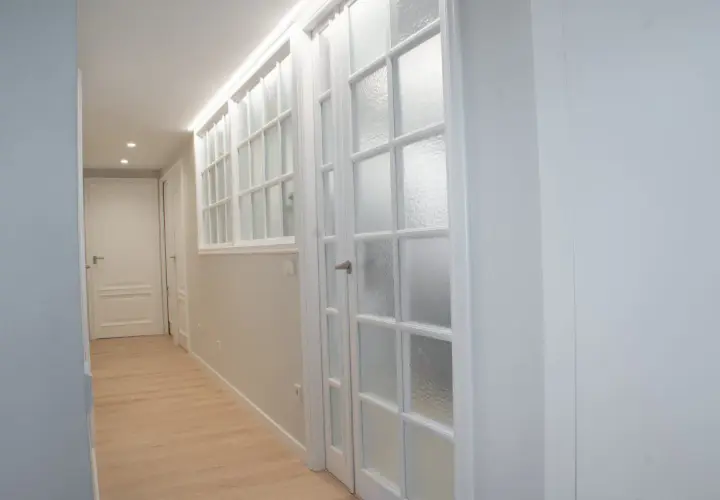 Pasillo con puertas blancas y vidrios emplomados, destacando la variedad de **colores de puertas** en un diseño moderno y luminoso.