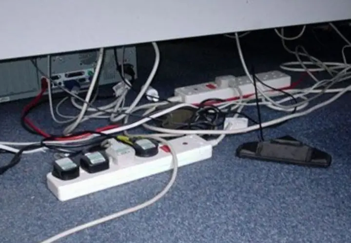 Un enredo de cables y regletas bajo un escritorio. Un ejemplo de qué es un contacto eléctrico indirecto, con cables expuestos y enchufes.