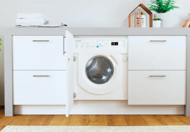 Lavadora Indesit con puerta abierta, lista para el lavado. El desague lavadora está oculto tras el mueble.