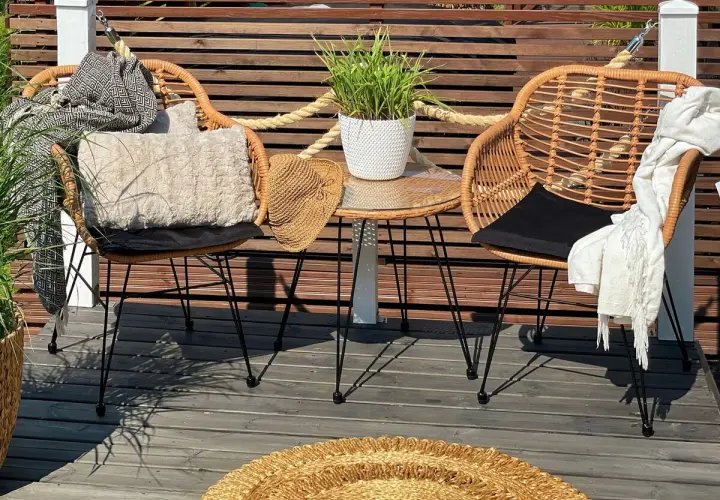 Dos sillas de mimbre con cojines y mantas, una mesa auxiliar con planta y un sombrero de paja. Decoración de mini balcones acogedora.