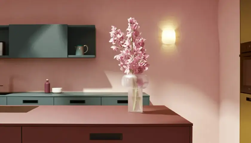 Elegante cocina con una **combinación de colores para cocina** audaz: rosa empolvado, verde azulado y detalles en burdeos y ocre. Flores rosas en un jarrón.