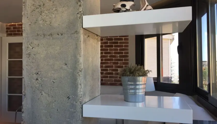 Ideas para decorar columnas dentro de la casa: estantes blancos flotantes con un modelo de Vespa y una planta en lata.