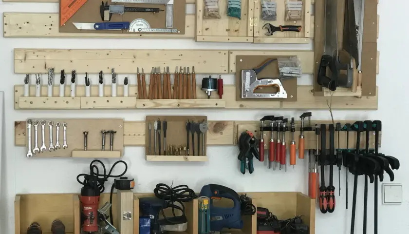 Organizar herramientas casero: un panel de madera con sierras, taladros, llaves, destornilladores y más, todo ordenado.