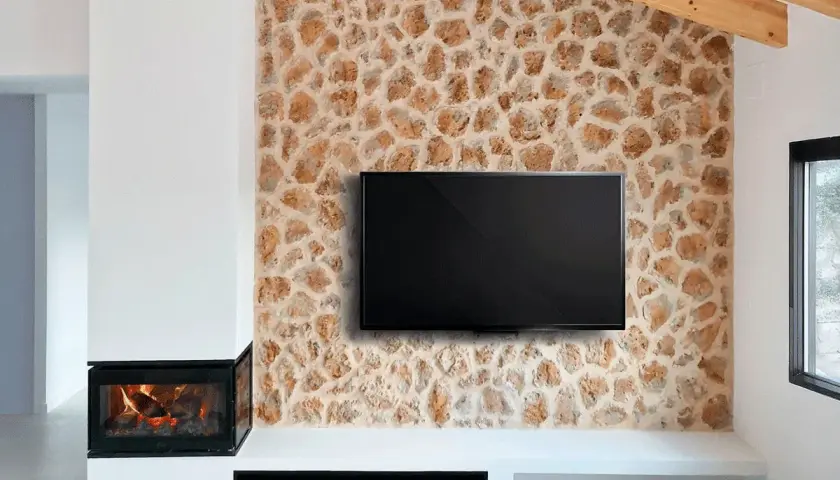 Televisor colgado sobre una pared con un rústico revestimiento de piedra natural, junto a una chimenea moderna.