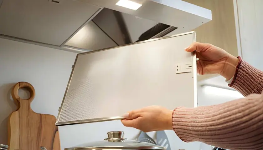 Manos desmontando el filtro de una campana extractora antigua para limpiarla.
