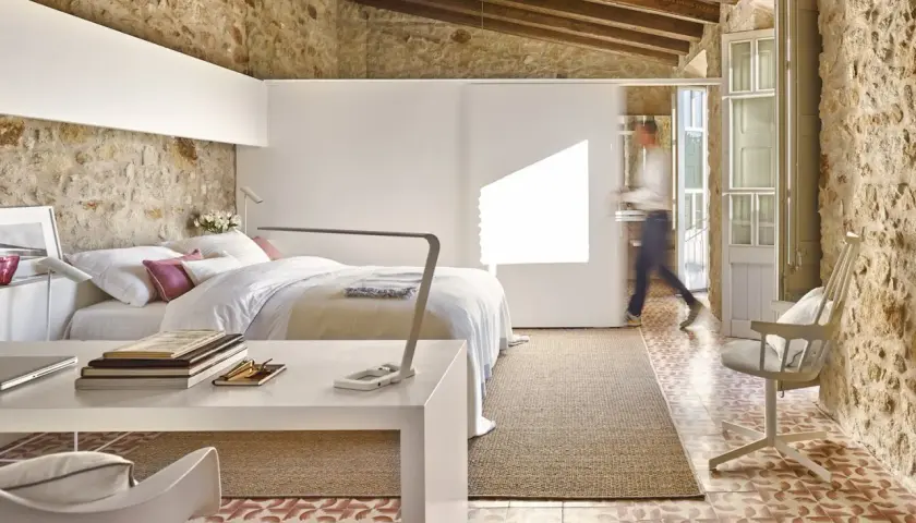 Habitación con cama, escritorio y una persona caminando. Usa paredes falsas para separar espacios, integrando piedra rústica y diseño moderno.