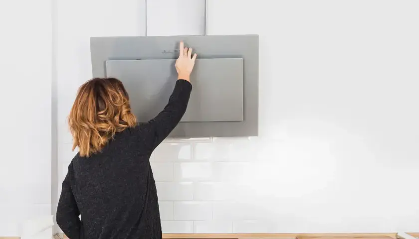 Mujer toca panel de control de campana extractora moderna, lista para cambiarla o limpiarla.