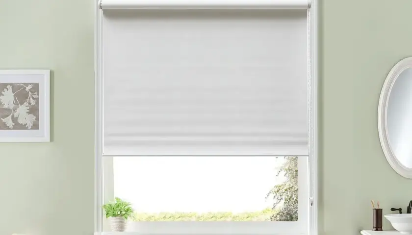 Ventana con estor enrollable blanco, ideal para aprender cómo hacer un estor. Al lado, un cuadro y toallas.