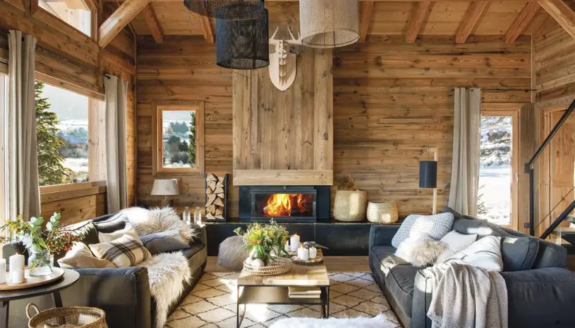 Acogedor salón con chimenea encendida, sofás grises, alfombra de rombos y mucha madera. La decoración casa rústica perfecta para el invierno.