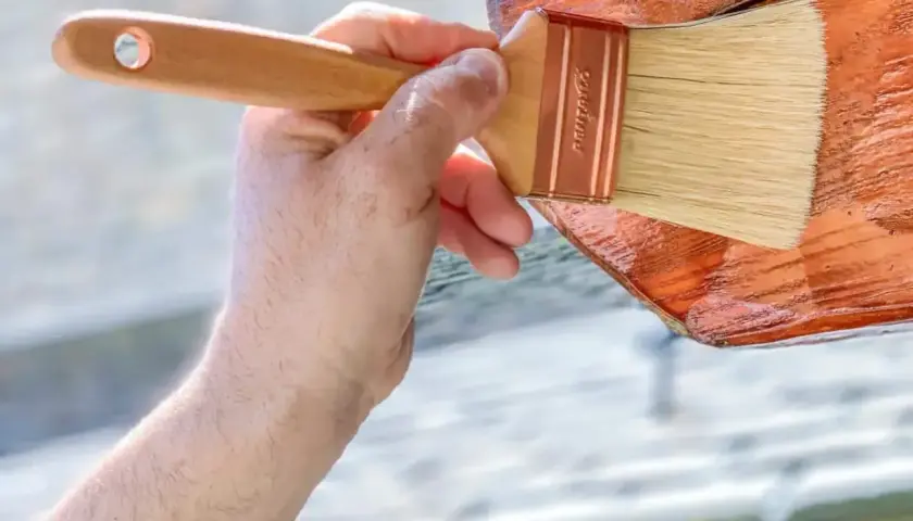 Aplicando el mejor tratamiento para la madera exterior. Una mano con brocha protege la madera, dándole un acabado brillante y duradero.