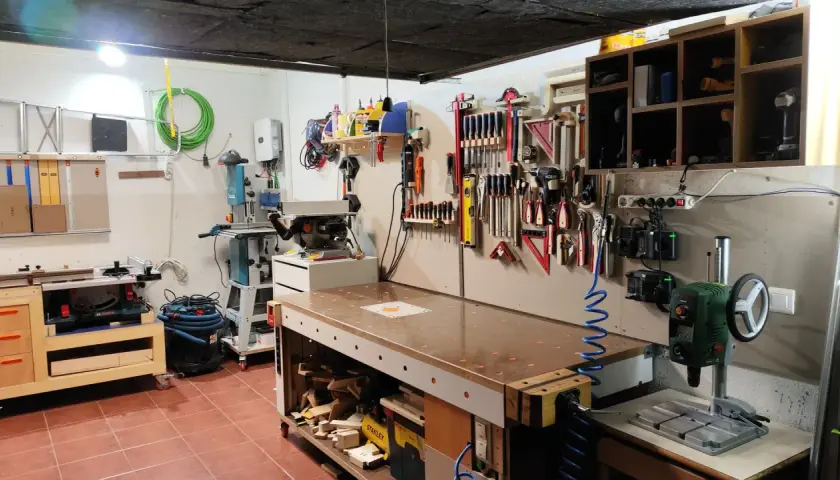 Un completo taller en casa con banco de trabajo, sierra de calar, taladro de columna y herramientas organizadas en la pared.