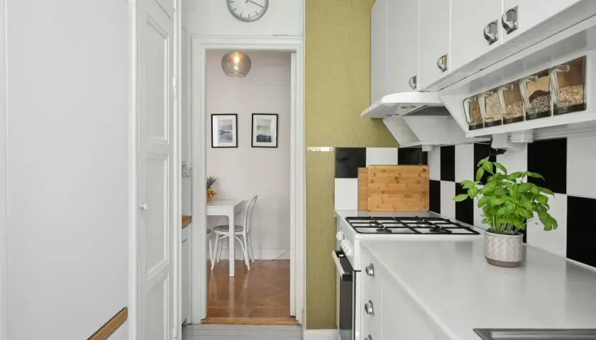 Cocina blanca y ordenada con estantes transparentes para organizar alimentos. Al fondo, un comedor pequeño.