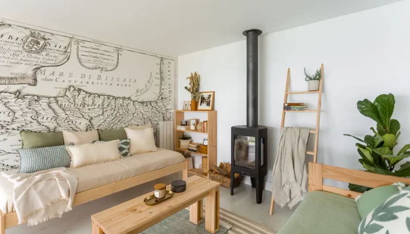 Acogedora sala de estar pequeña sencilla con sofá de madera, chimenea, estantería y un mapa antiguo en la pared.