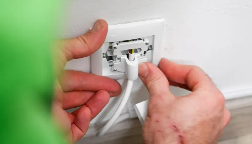 Manos conectando un cable a un enchufe para instalar enchufe de superficie.