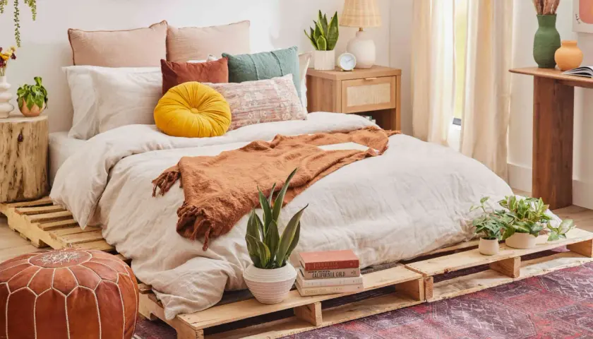 Cama acogedora con cómodas camas hechas con palets, cojines coloridos y manta naranja.