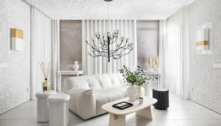 Salón minimalista con sofá blanco, mesa de centro ovalada y **gotele moderno** en paredes y techo. Lámpara escultural y cortinas blancas completan el espacio.