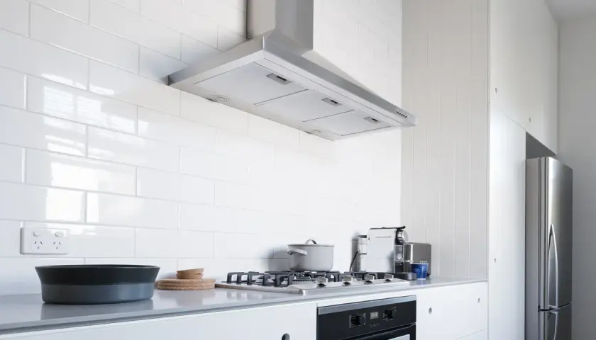 Cocina moderna con campana extractora de acero inoxidable, una de las muchas tipos de campanas extractoras. Encimera gris, vitrocerámica y nevera.