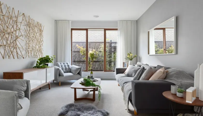 Salón moderno con sofás grises, mesa de centro de madera y arte de pared de ramas. Las paredes color gris crean un ambiente sereno.
