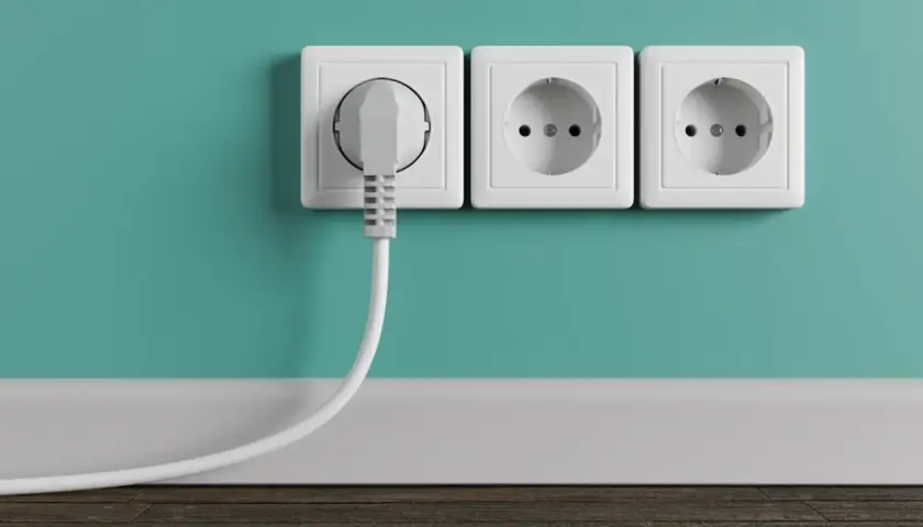 Tres enchufes blancos en una pared turquesa. Uno tiene un enchufe gris conectado. La altura de los enchufes en la cocina es estándar.