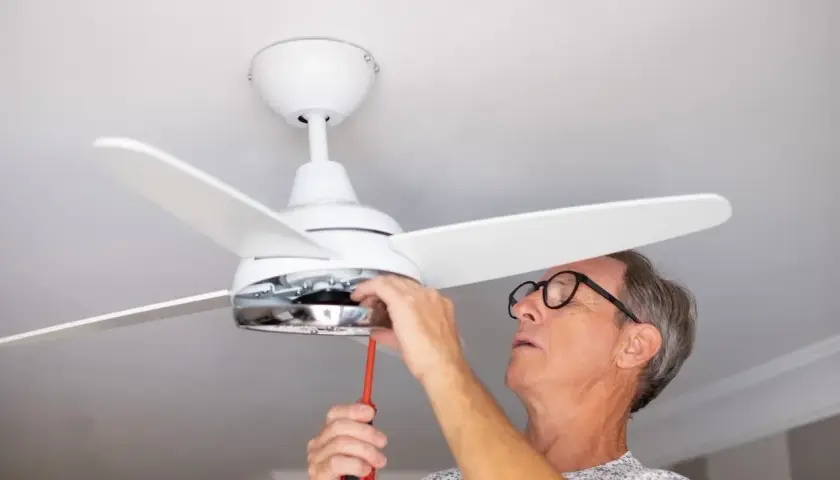 Hombre con gafas ajusta un ventilador de techo pladur con un destornillador.