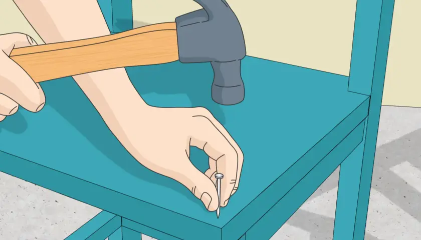 Manos martillando un clavo en una silla de madera azul. Paso a paso, como hacer una silla de madera.