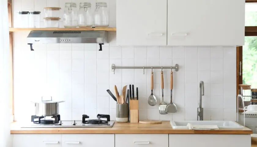 Una cocina pequeña y luminosa con encimera de madera, utensilios colgados y un fregadero.