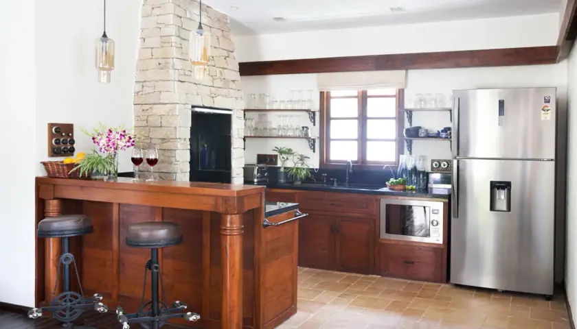 Cocinas con chimenea de piedra, barra de madera con taburetes, electrodomésticos de acero inoxidable y ventana rústica.