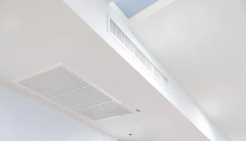 Rejillas de aire acondicionado integradas en un falso techo blanco, con conductos ocultos para una climatización discreta.