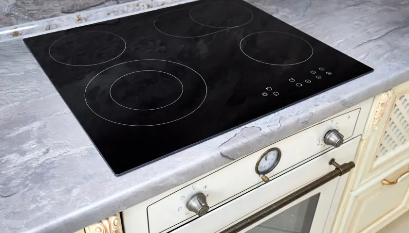 Placa de cocina vitrocerámica negra con cuatro zonas de calor y controles táctiles. Encimera gris piedra.