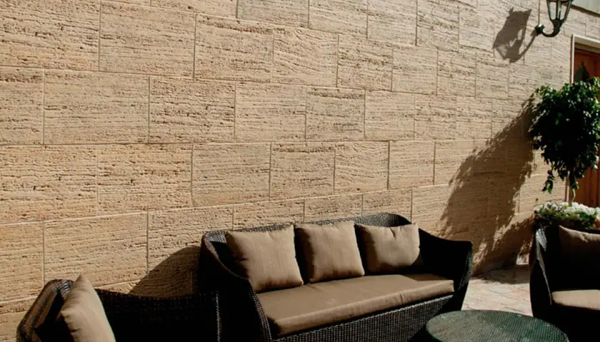 Un patio acogedor con muebles de mimbre y cojines marrones, rodeado de patios con paredes de piedra natural.