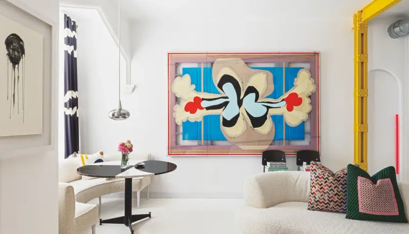 Un salón moderno con arte abstracto y muebles curvos. Sofás blancos texturizados y una mesa redonda negra y blanca crean sencillas salas pequeñas.